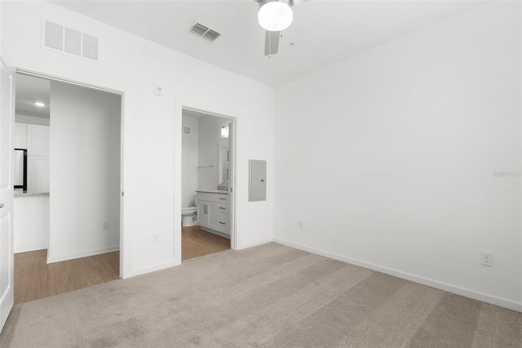 A carpeted bedroom features a ceiling fan, a doorway to a bathroom, and a kitchen view — 1700 RANCH ROAD UNIT A3-2116, NOKOMIS, FL