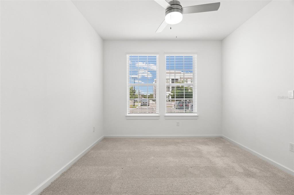 A bright, empty bedroom features white walls, beige carpeting, a ceiling fan, and two windows — 1700 RANCH ROAD UNIT A3-2116, NOKOMIS, FL