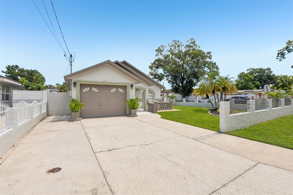 A single-story house with a beige garage, concrete driveway, and a white perimeter fence — 7001 N CLARK AVENUE, TAMPA, FL