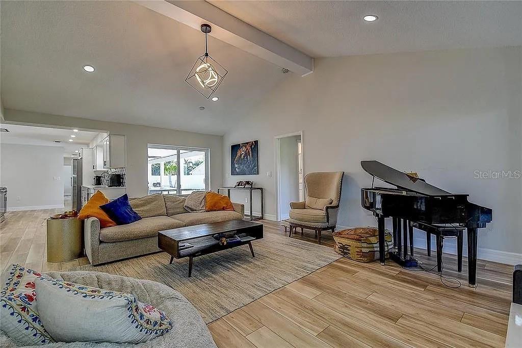 A living room features a beige sofa, a grand piano, and light wood-look flooring — 4723 THOMAS HOBY PLACE, SARASOTA, FL