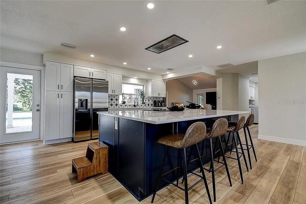 A modern kitchen features a large dark blue island with bar stools and white cabinetry — 4723 THOMAS HOBY PLACE, SARASOTA, FL