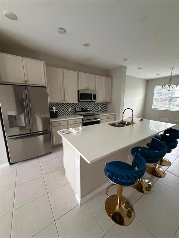 A kitchen features white cabinets, stainless steel appliances, a large island, and blue velvet stools — 11165 LIME FLOWER DRIVE, WINTER GARDEN, FL