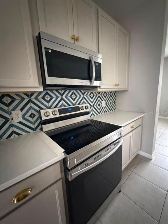 A kitchen features white cabinets, stainless steel appliances, and a blue and white patterned backsplash — 11165 LIME FLOWER DRIVE, WINTER GARDEN, FL