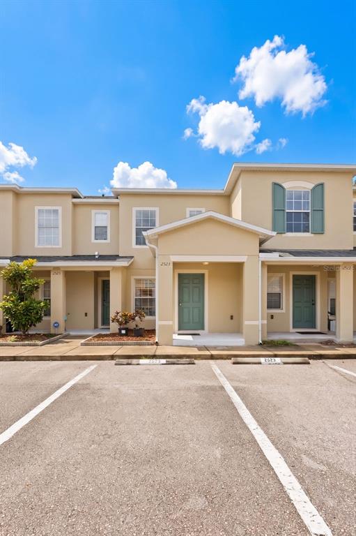 A multi-story townhouse exterior features tan stucco walls, green doors, and a paved parking area — 2523 SANDY BEACH LANE, CLEARWATER, FL