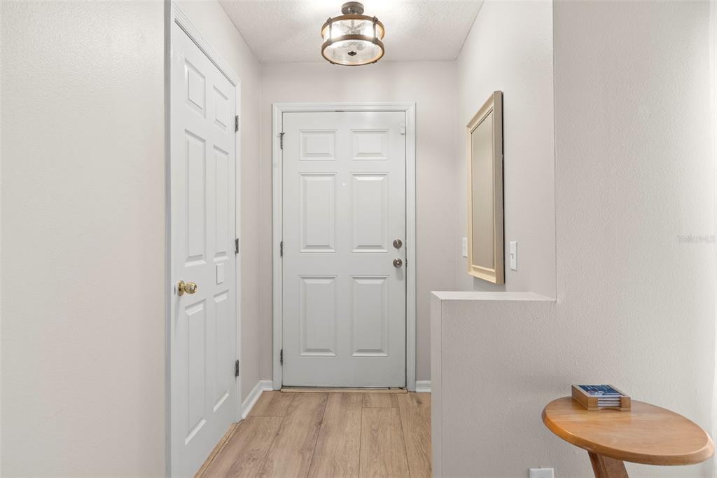 A bright entryway features light wood-look flooring, a white front door, and a small side table — 2523 SANDY BEACH LANE, CLEARWATER, FL