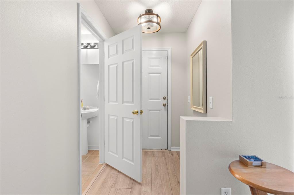 A hallway features light wood-look flooring, a flush-mount light fixture, and a white interior door — 2523 SANDY BEACH LANE, CLEARWATER, FL