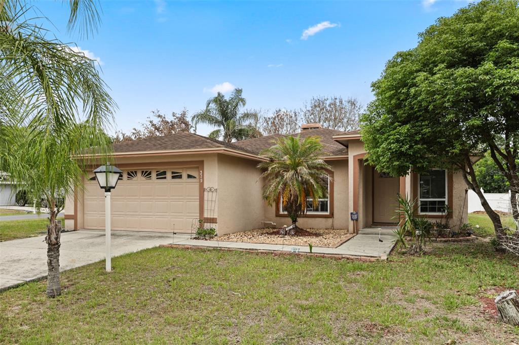 A single-story house with a tan stucco exterior, a two-car garage, and a front lawn — 329 LAKE DAISY LOOP, WINTER HAVEN, FL