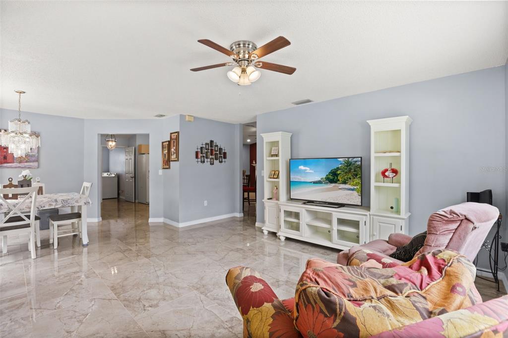 A living room with light blue walls, tile flooring, a ceiling fan, and white shelving — 329 LAKE DAISY LOOP, WINTER HAVEN, FL