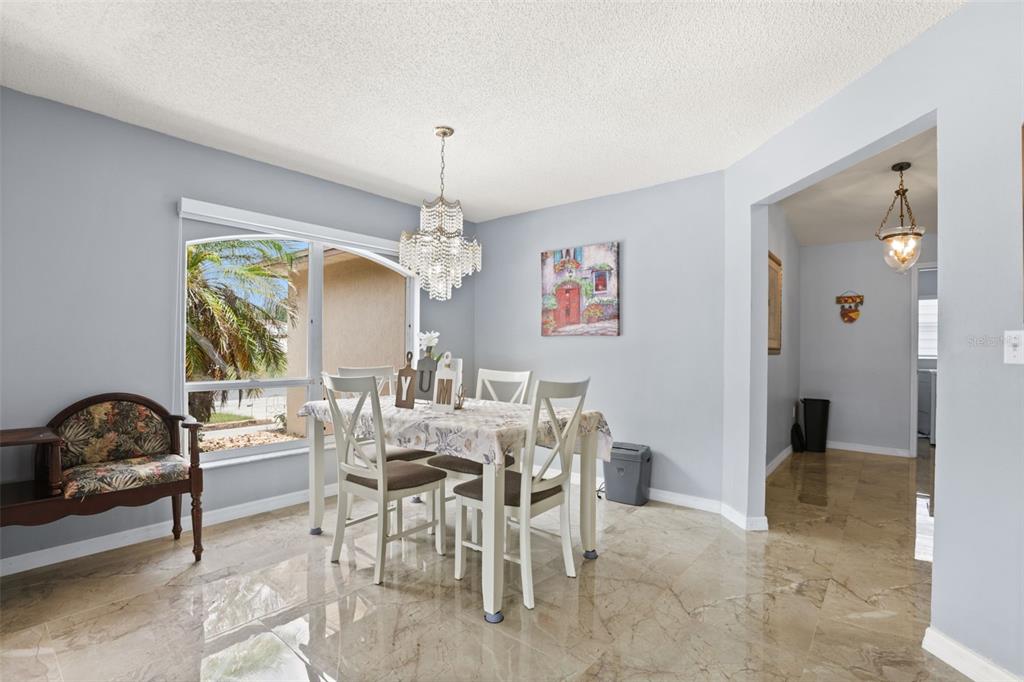 A dining room with a crystal chandelier, white table and chairs, and light-colored tile floors — 329 LAKE DAISY LOOP, WINTER HAVEN, FL