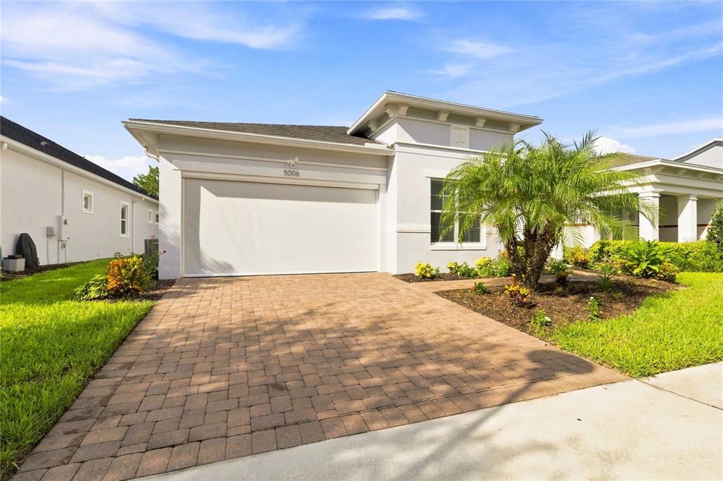 A single-story house features a paved driveway, a closed garage door, and a palm tree — 5006 E FOUNTAINWOOD DRIVE, ST CLOUD, FL