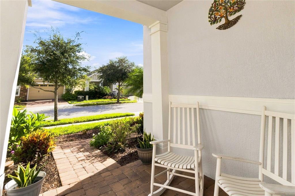 A covered front porch features two white rocking chairs and a decorative metal tree wall hanging — 5006 E FOUNTAINWOOD DRIVE, ST CLOUD, FL