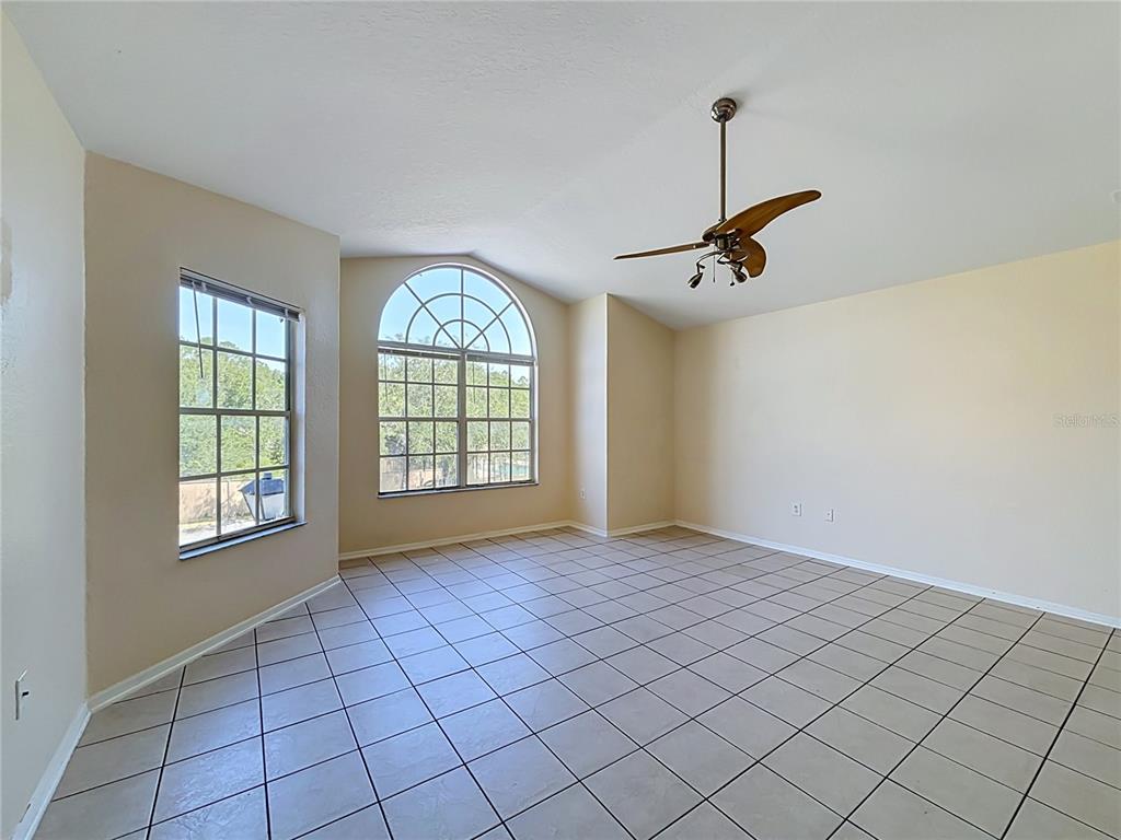 An empty room features beige walls, tiled floors, a ceiling fan, and large arched windows — 2332 PRIME CIRCLE UNIT B, KISSIMMEE, FL