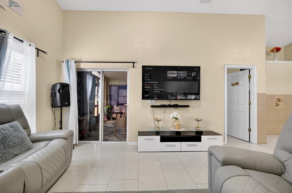 A living room features light-colored tile floors, a wall-mounted television, and a sliding glass door — 4524 SETTLEMENT CIRCLE, ORLANDO, FL