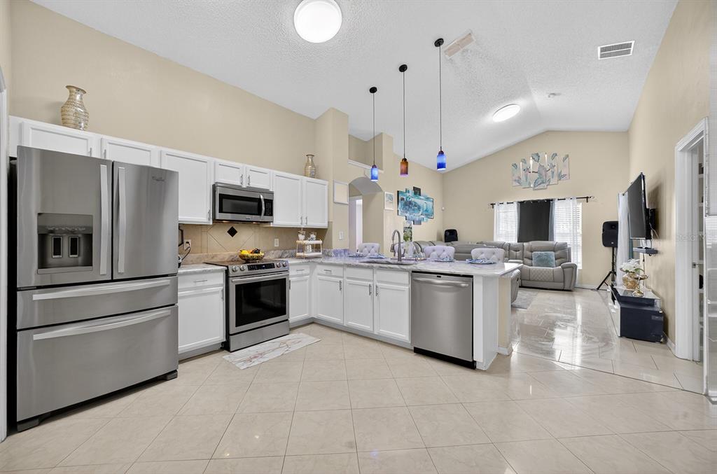 A kitchen with white cabinets, stainless steel appliances, and tile flooring opens to a living area — 4524 SETTLEMENT CIRCLE, ORLANDO, FL