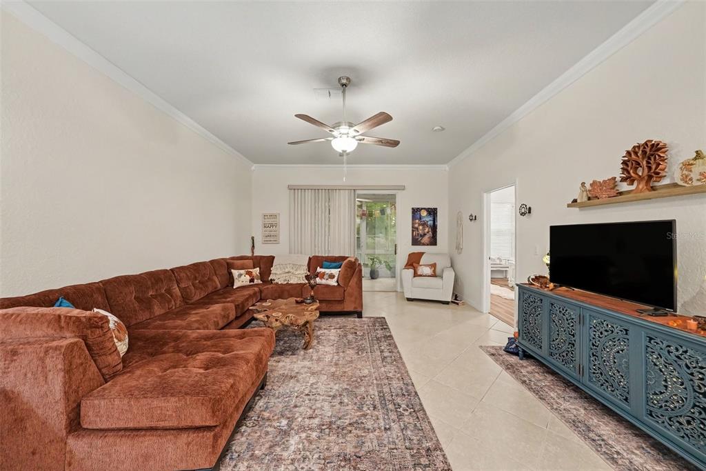 A living room features a large brown sectional, a blue media console, and a ceiling fan — 12126 TOURNAMENT VIEW AVE, NEW PORT RICHEY, FL