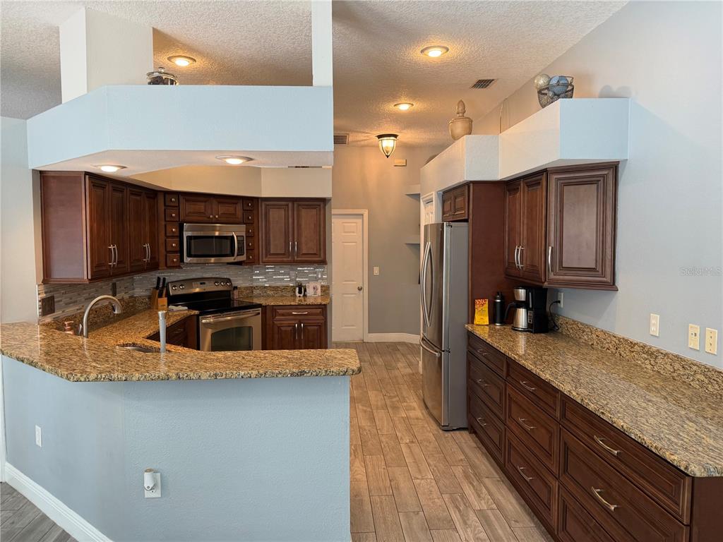 A kitchen features dark wood cabinets, granite countertops, stainless steel appliances, and light blue walls — 1616 KINSMERE DRIVE, TRINITY, FL