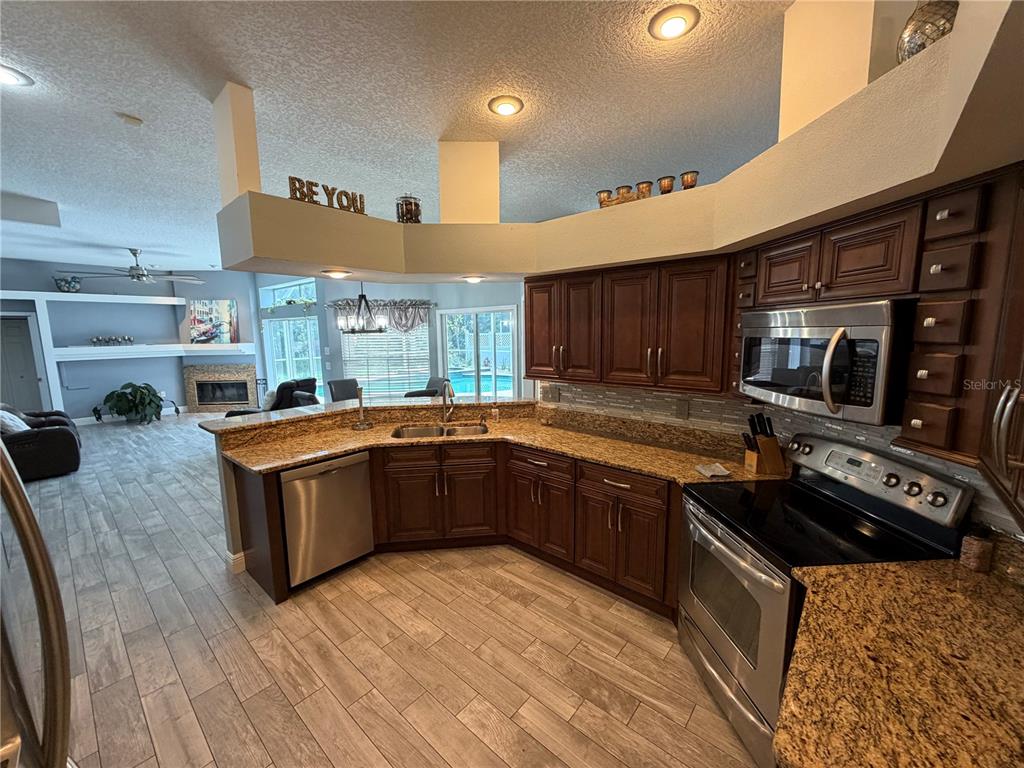 A kitchen with dark wood cabinets, granite countertops, and stainless steel appliances overlooks a living area — 1616 KINSMERE DRIVE, TRINITY, FL