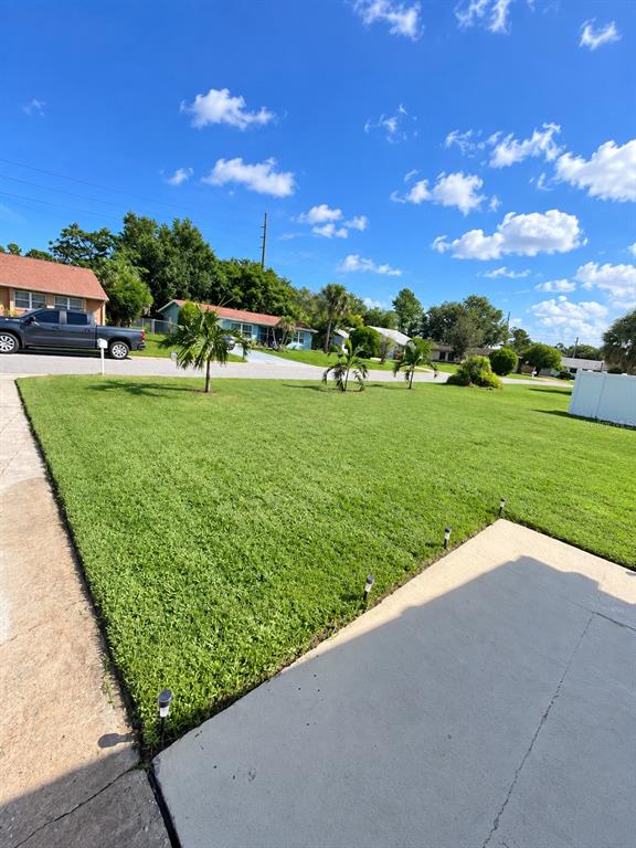 A grassy backyard features a white vinyl fence, a partial pool, and a house exterior — 17 S FLAG DRIVE, KISSIMMEE, FL