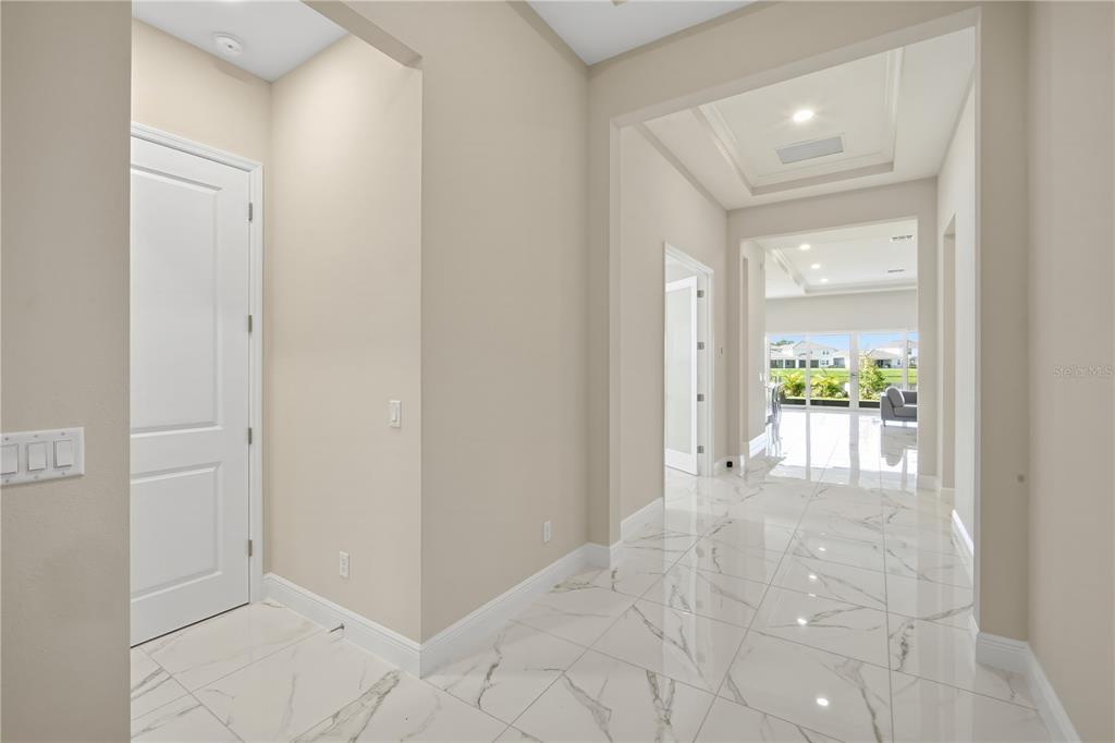 A bright foyer with white marble-look tile flooring leads toward a sunlit living area — 9632 SURREY ROSE DRIVE, SAN ANTONIO, FL