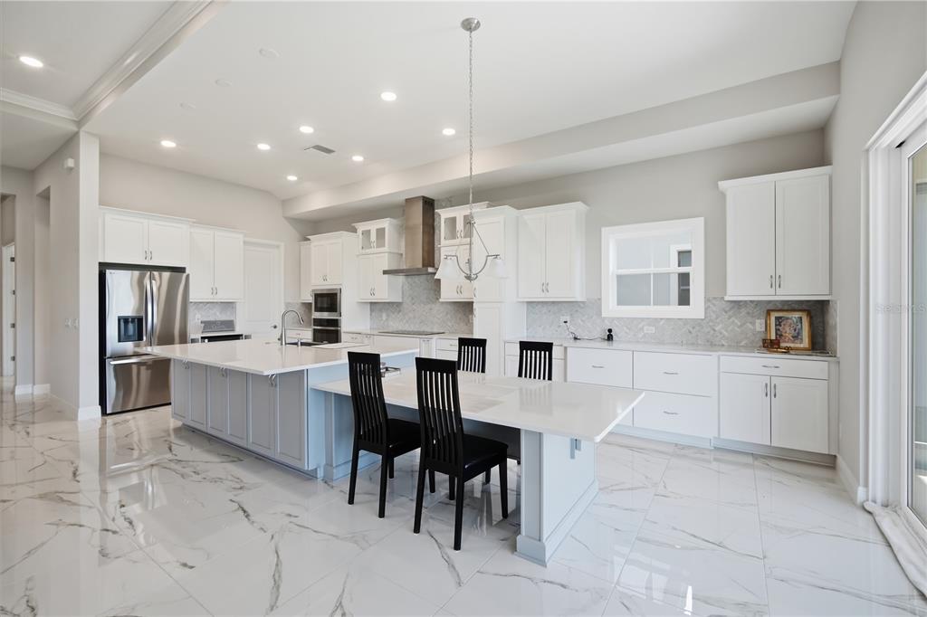 A modern kitchen features white cabinetry, a large island with seating, and marble-patterned tile flooring — 9632 SURREY ROSE DRIVE, SAN ANTONIO, FL