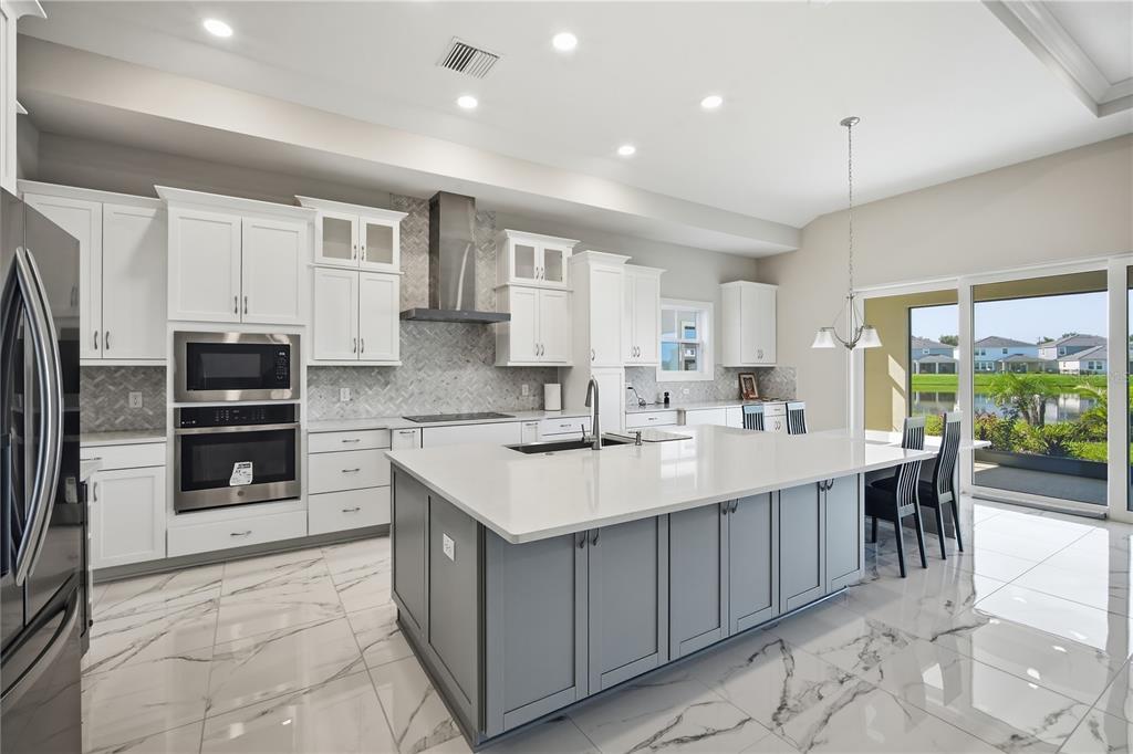 A modern kitchen features white cabinets, a gray island with a white countertop, and tile flooring — 9632 SURREY ROSE DRIVE, SAN ANTONIO, FL