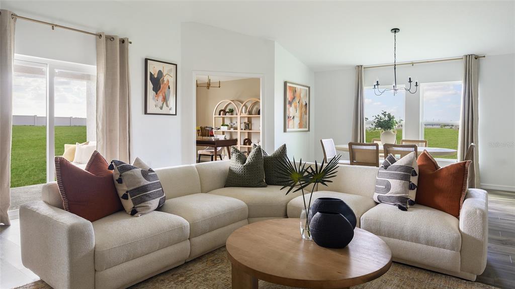 A bright living room features a large cream sectional sofa, a round wooden coffee table, and dining area — 3907 ALTITUDE RUN, DAVENPORT, FL