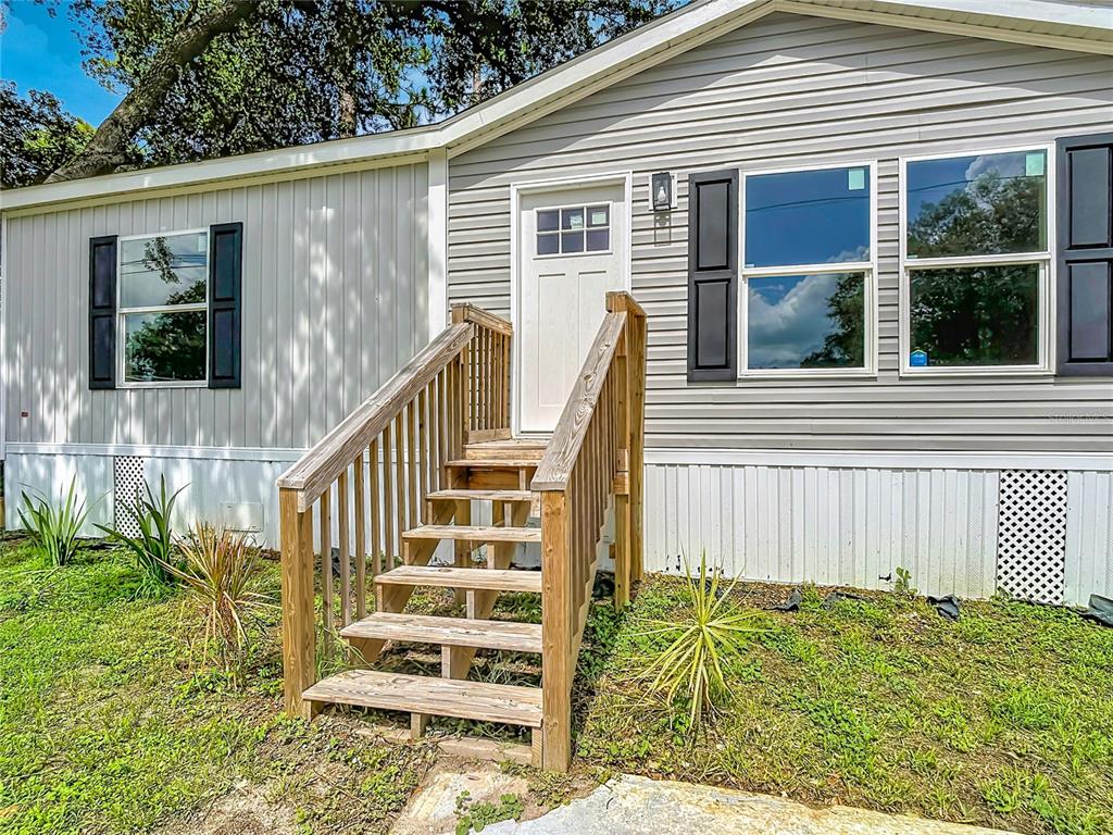 A light gray mobile home exterior features a wooden staircase leading to the front door — 1657 FLOUNDER STREET, ST CLOUD, FL