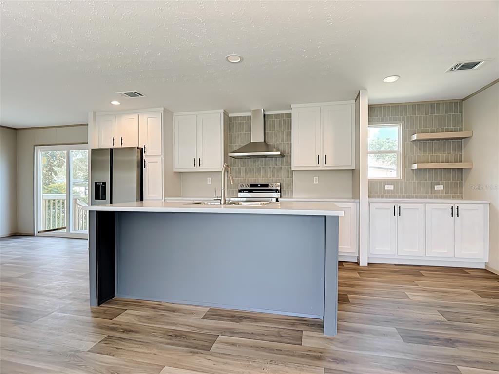 A modern kitchen features white cabinets, a blue island, stainless steel appliances, and wood flooring — 1657 FLOUNDER STREET, ST CLOUD, FL