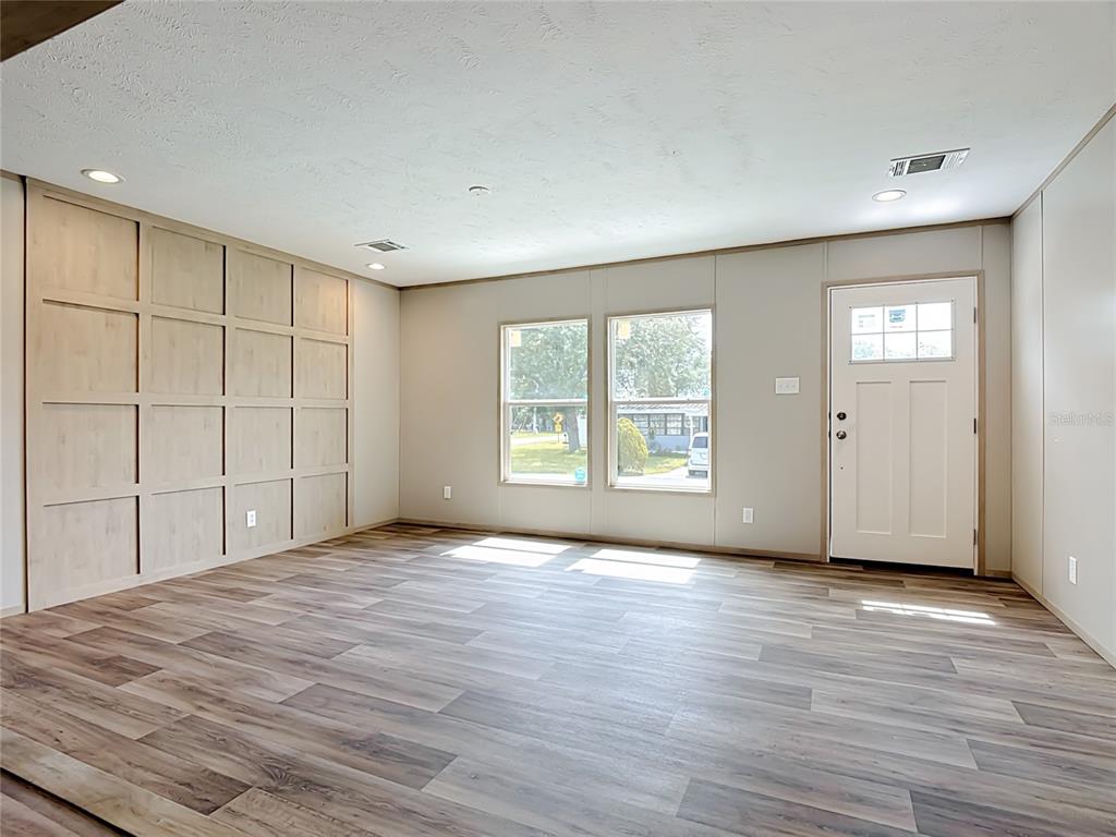 An empty room features wood-look flooring, a paneled accent wall, two windows, and an entry door — 1657 FLOUNDER STREET, ST CLOUD, FL