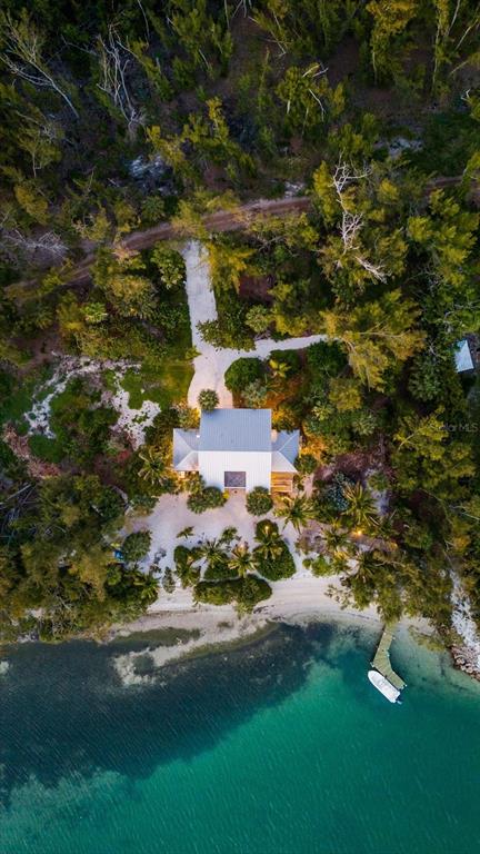 An aerial view shows a house nestled in a wooded area beside a turquoise bay — 7143 LA LENAIRE DRIVE, LONGBOAT KEY, FL