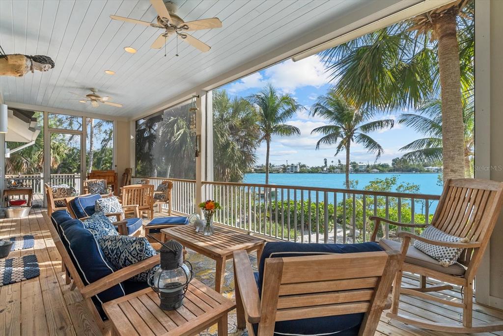 A screened-in wooden porch features outdoor furniture overlooking a blue bay and palm trees — 7143 LA LENAIRE DRIVE, LONGBOAT KEY, FL