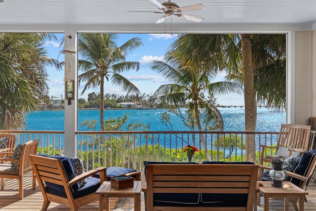 A screened-in porch with wood furniture overlooks a tropical waterfront view with palm trees — 7143 LA LENAIRE DRIVE, LONGBOAT KEY, FL