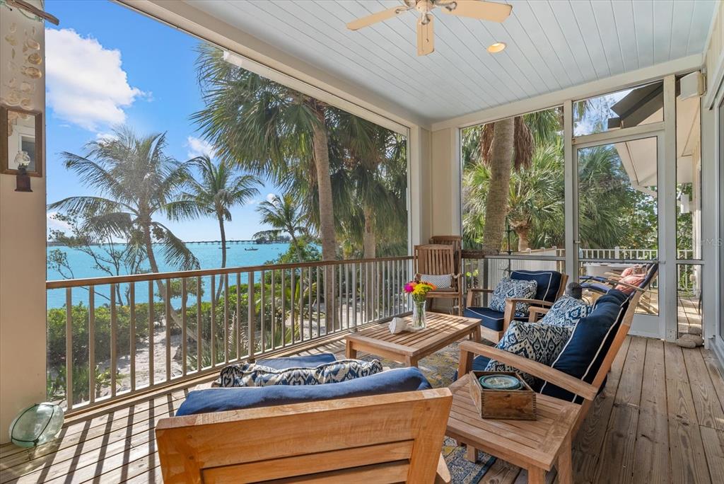 A screened-in porch features wooden furniture, a ceiling fan, and a view of the ocean — 7143 LA LENAIRE DRIVE, LONGBOAT KEY, FL
