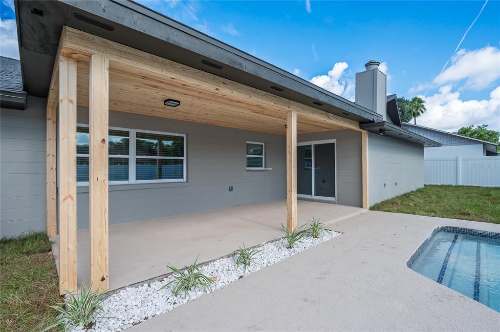 A covered patio with wood ceiling and support posts overlooks a swimming pool and yard — 5112 JEANNINE COURT, ORLANDO, FL