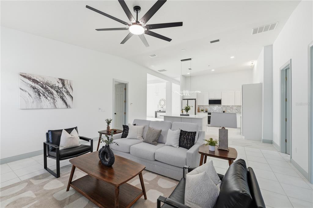 A modern living room with a grey sofa, black chairs, and an open-concept kitchen — 4873 NE 64 AVENUE, SILVER SPRINGS, FL