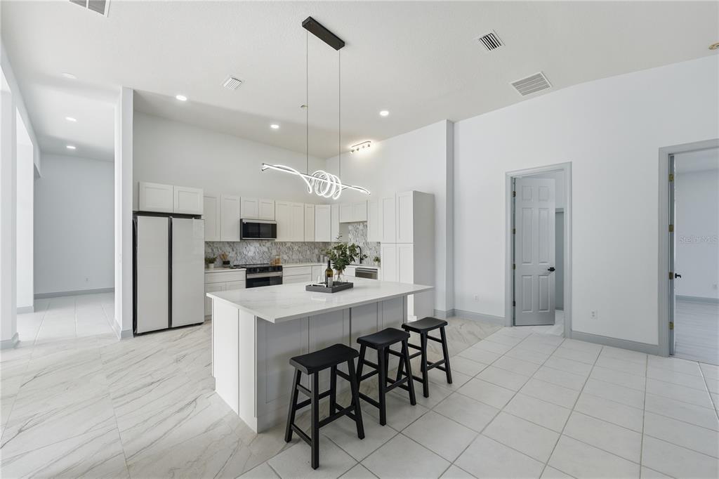 A modern white kitchen features a central island with bar stools and marble-patterned tile flooring — 4873 NE 64 AVENUE, SILVER SPRINGS, FL