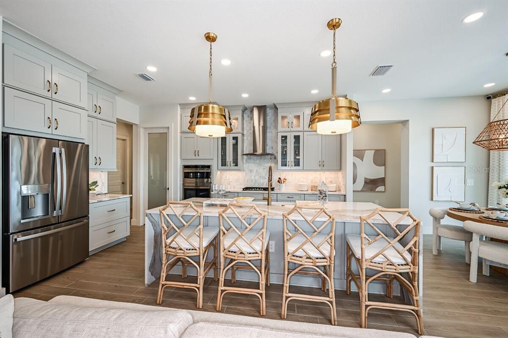 A modern kitchen features light gray cabinets, a marble island, and four rattan bar stools — 17524 MACARTHUR LOOP, VENICE, FL