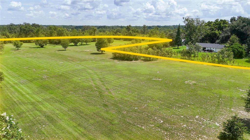 An aerial view shows a large, grassy field with scattered trees and a distant house — 2452 WELCOME ROAD, LITHIA, FL