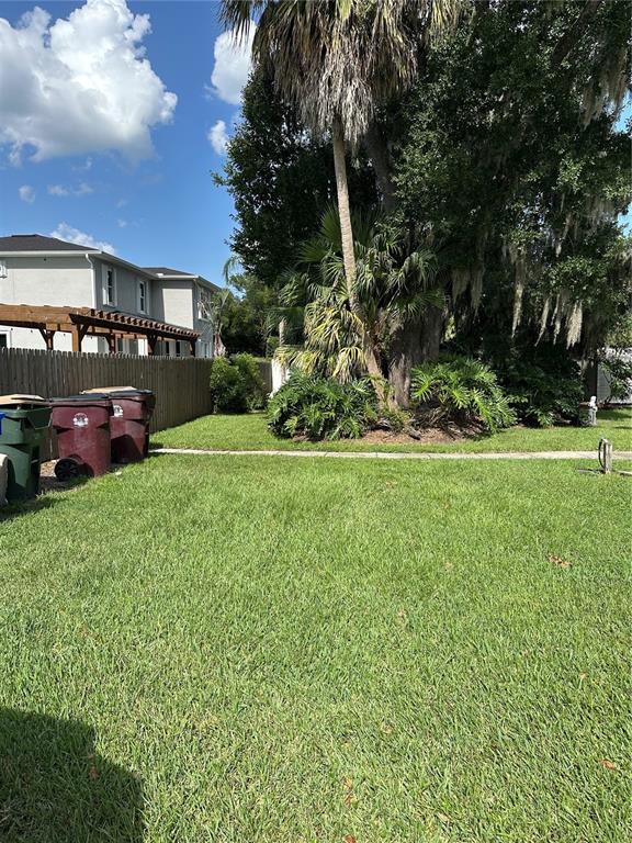 A grassy backyard features a wooden fence, several trash bins, and large palm trees — 3430 5TH STREET, ST CLOUD, FL