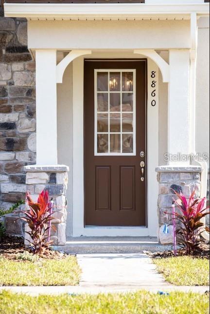 A brown front door with a glass window pane is framed by stone pillars and plants — 8860 HERENCIA ALLEY, WINDERMERE, FL