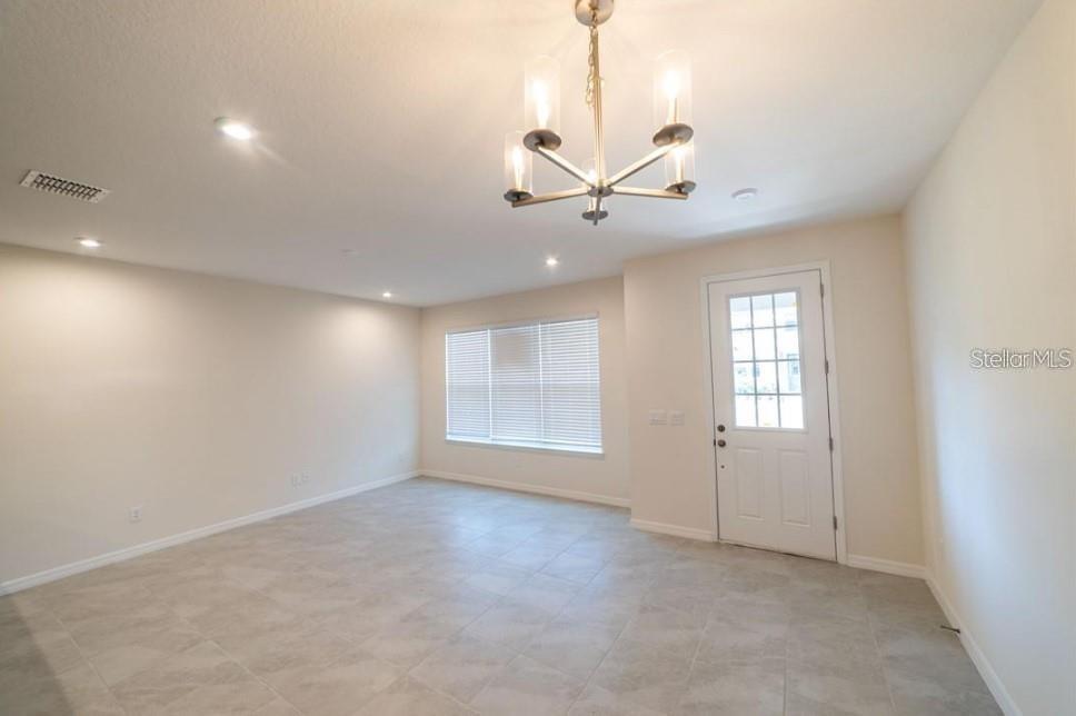An empty room features light-colored tile flooring, a modern chandelier, and a white exterior door — 8860 HERENCIA ALLEY, WINDERMERE, FL