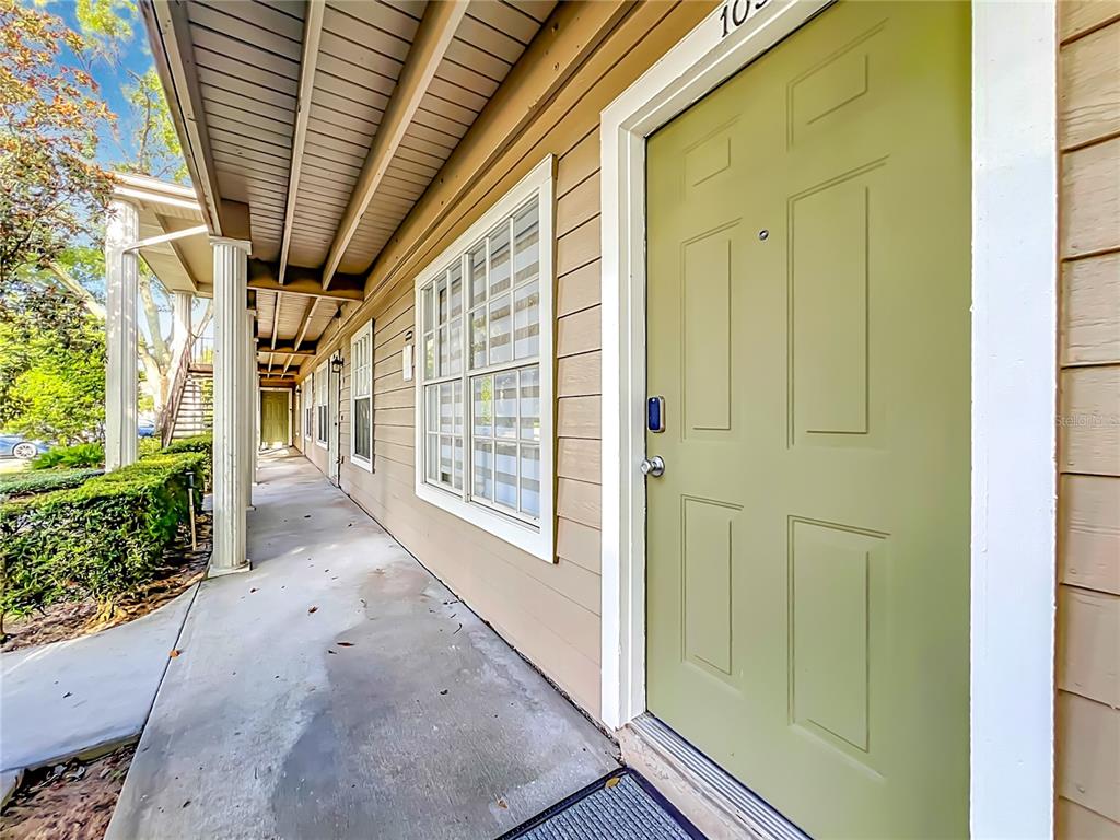 A light green front door opens onto a covered concrete walkway lined with white columns — 121 RESERVE CIRCLE UNIT 105, OVIEDO, FL