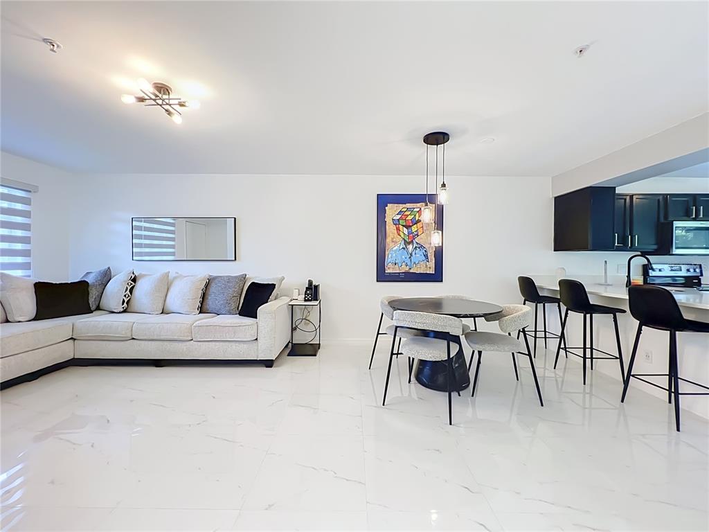 A modern open-concept living and dining area features white tile floors, a sectional sofa, and kitchen bar seating — 121 RESERVE CIRCLE UNIT 105, OVIEDO, FL