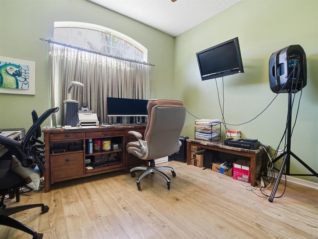 A home office features light green walls, wood-look flooring, a desk, and a mounted television — 24511 BOCAGE WAY, LEESBURG, FL