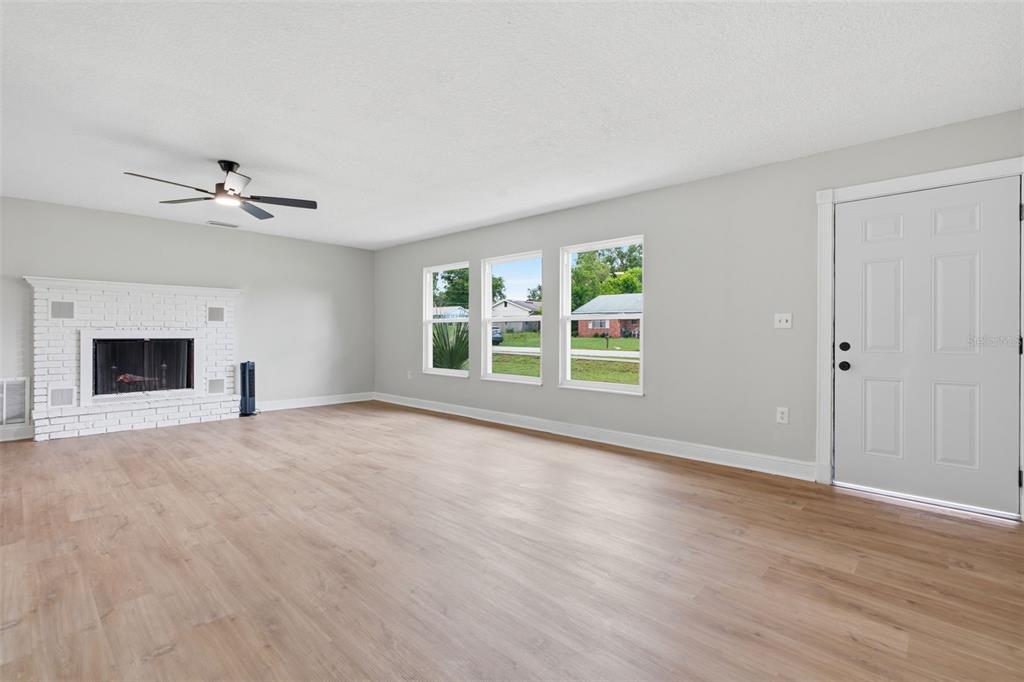A living room with light wood flooring, a white brick fireplace, and a front door — 147 COLOMBA ROAD, DEBARY, FL