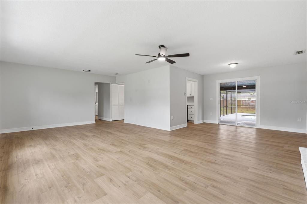 An open-concept living area features light wood-look flooring, a ceiling fan, and sliding glass doors — 147 COLOMBA ROAD, DEBARY, FL