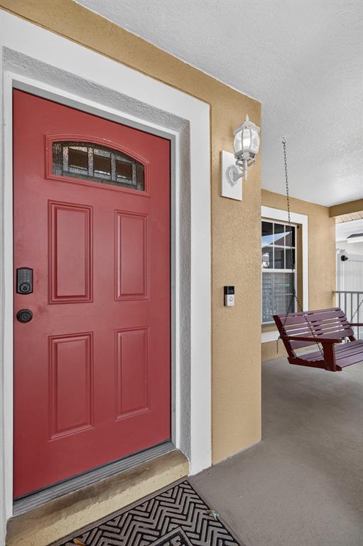 A red front door with a window sits beside a porch swing and wall light — 1742 HORSECHESTNUT COURT, NEW PORT RICHEY, FL