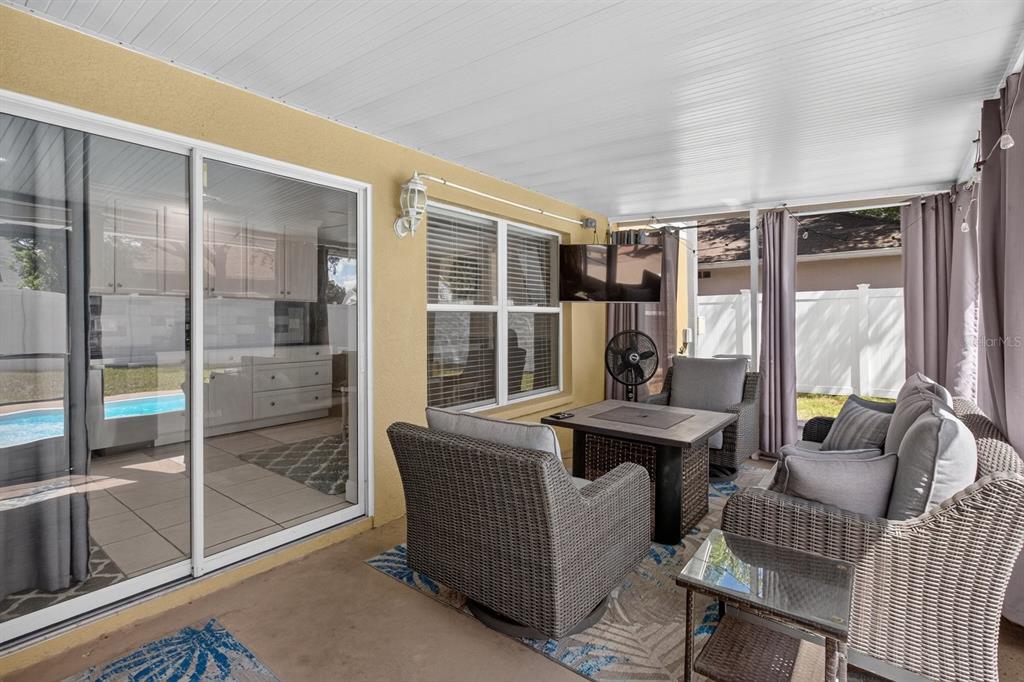 A covered patio features wicker furniture, a fire pit table, and sliding glass doors to indoors — 1742 HORSECHESTNUT COURT, NEW PORT RICHEY, FL