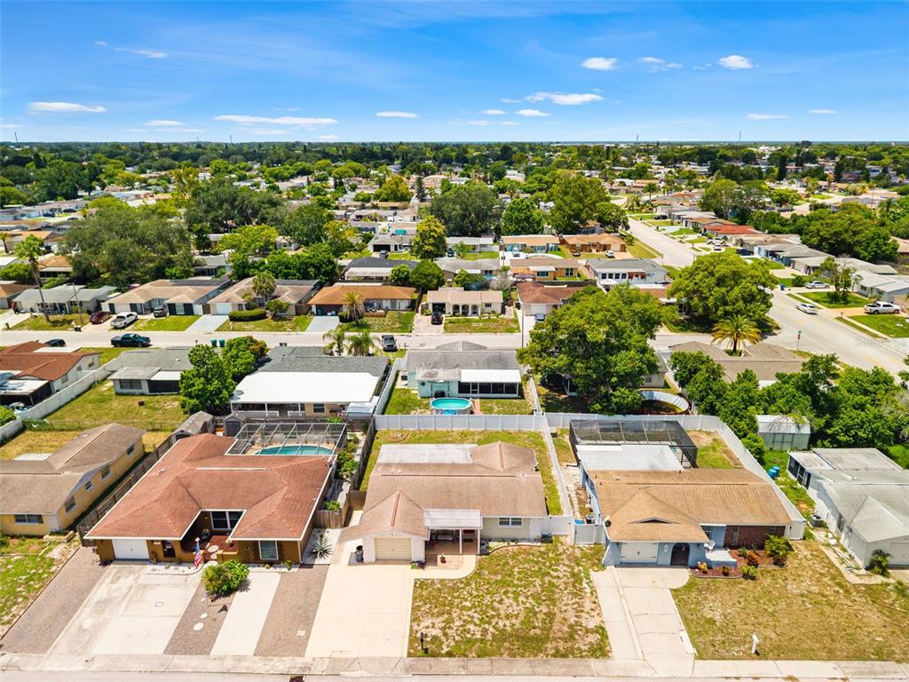 An aerial view shows three suburban houses with pools and driveways in a residential neighborhood — 9135 HERMITAGE LANE, PORT RICHEY, FL