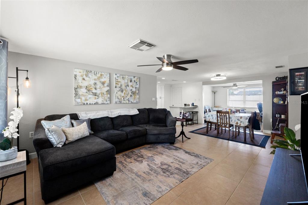 A living room with a dark sectional sofa, tile flooring, and an adjacent dining area — 9135 HERMITAGE LANE, PORT RICHEY, FL